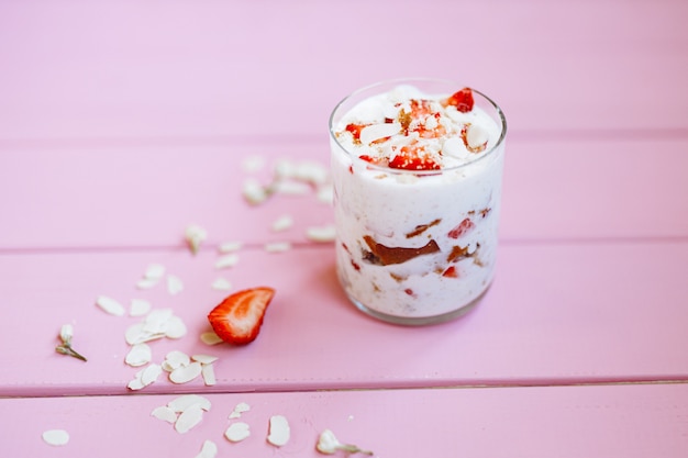 gelaagd zomerdessert met aardbeien, biscuitgebak en yoghurt op een roze boomachtergrond.