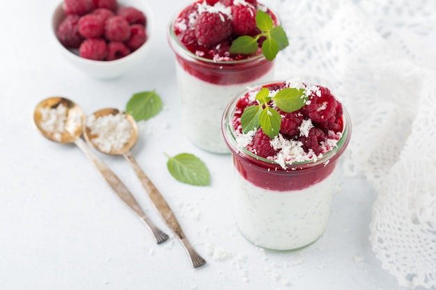 Gelaagde frambozensmoothies met chiazaad, verse framboos en kokos op een lichte pit. Handig toetje.