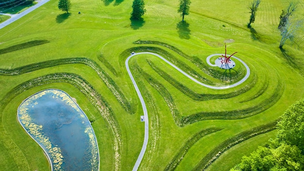 Gelaagde met gras begroeide heuvels met abstracte kunstsculpturen en een vijver onder een drone-opname van Ariel Foundation Park