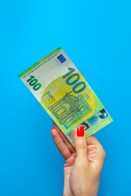 Geld in de hand, bankbiljet in de hand. Hand met 100 euro biljet op blauwe achtergrond.