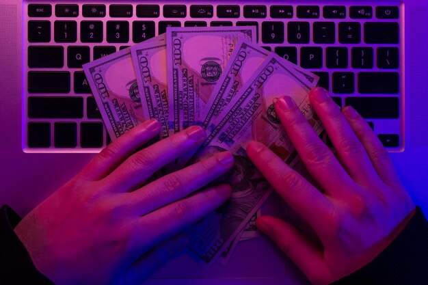 Foto geld in mannelijke handen op de achtergrond van een laptoptoetsenbord in neonverlichting