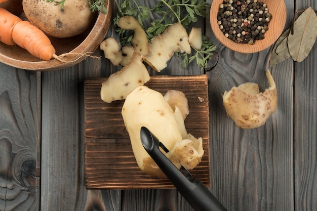 Gele aardappel schillen met dunschiller Plat lag weergave Verse rauwe aardappel Scherpe schil op houten keukenplank