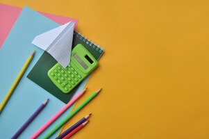 Foto gele achtergrond met schoolbenodigdheden potloden, papier, rekenmachine, notitieblok