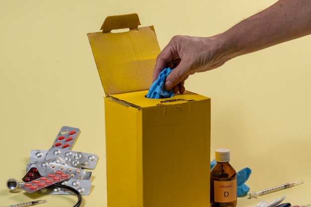 Gele afvalbak voor besmette of besmettelijke producten in een ziekenhuis of thuis. Hand die een beschermende handschoen zet