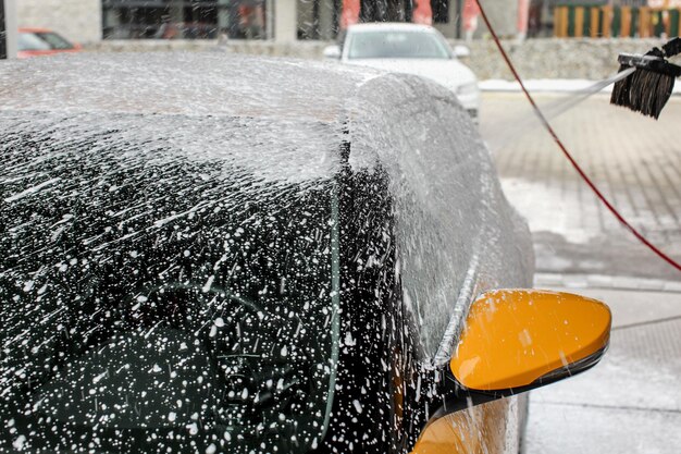 Gele auto bijna volledig bedekt met shampooschuim, met meer sproeien, wanneer gewassen in de wasstraat.