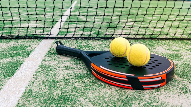 Gele bal bovenop het padelracket en achter het net op groen grasveld