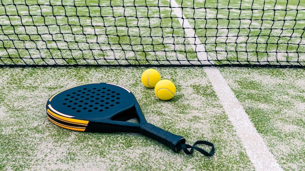 Gele ballen op grasgras dichtbij padeltennisracket achter net in groen hof