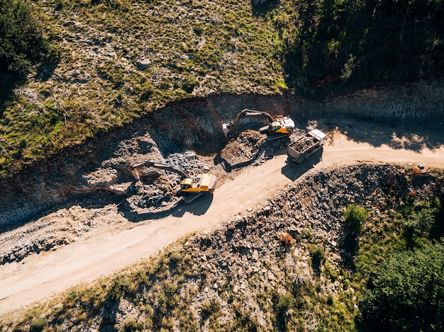 Gele bijgehouden tractor laadt een steengroeve voertuig met uitzicht op zand van drone