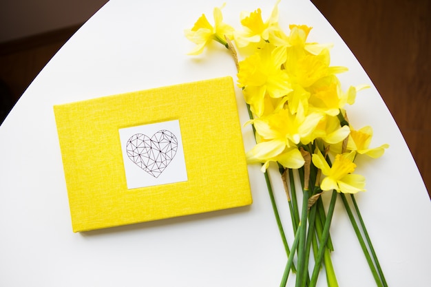 Gele boeket van narcissen en gele boek op witte tafel