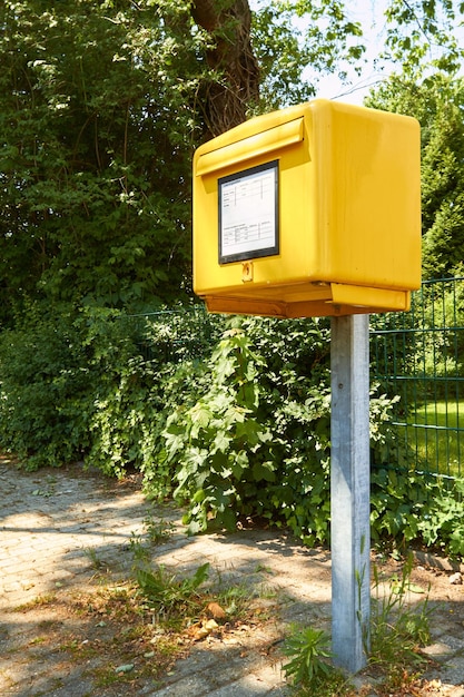 Gele brievenbus op voetpad tegen planten