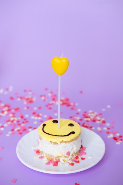 Gele cake smiley met een kaars in de vorm van een hart op een paarse achtergrond Valentijnsdag en verjaardag concept