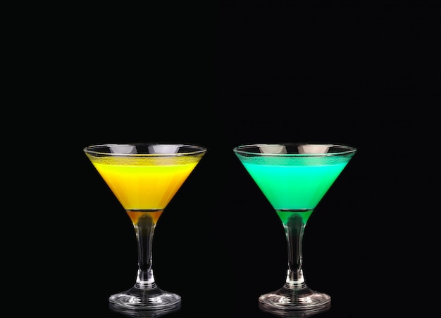 Gele en groene cocktail in martini-glas dat op zwarte wordt geïsoleerd