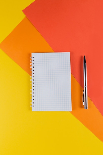 Gele en oranje bureaulijst met leeg notitieboekje en andere kantoorbenodigdheden. Bovenaanzicht met kopie ruimte, plat leggen.