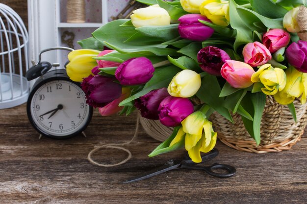 Gele en paarse verse tulp bloemen met retro klok op houten tafel