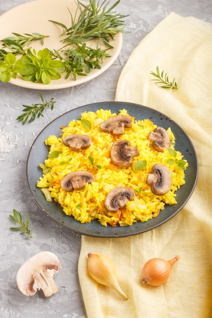 Gele gebakken rijst met champignons champignons, kurkuma en orego op blauwe keramische plaat op een grijze betonnen achtergrond