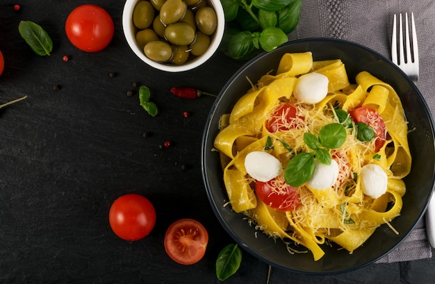 Gele gekookte pasta pappardelle, fettuccine of tagliatelle in zwarte kom bovenaanzicht.