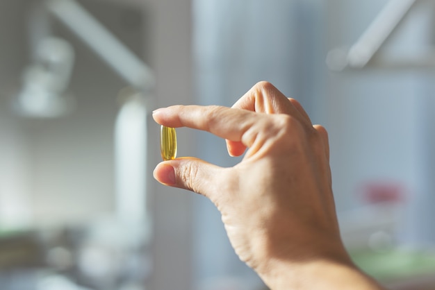 Gele gel capsule van vitamine D, E, omega-3 in dames hand close-up