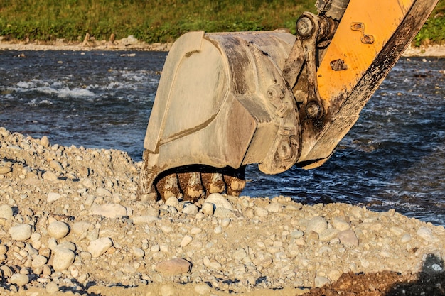 Gele graafmachine (graafmachine) emmer graven in stenen grond bij de rivier.