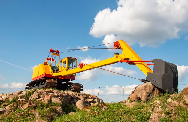 Gele graafmachine op stenen bouwplaats met zwarte emmer op een zonnige dag bouwconcept