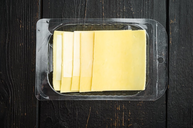 Foto gele kaas plakjes cheddar in plastic verpakking op zwarte houten tafel achtergrond bovenaanzicht plat lag