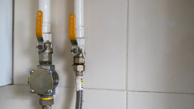 Gele kleppen en aardgasleidingen in een modern huisketelruim in een keuken met keramische tegels. gasklep kogelkraan, gas en sanitair apparatuur.