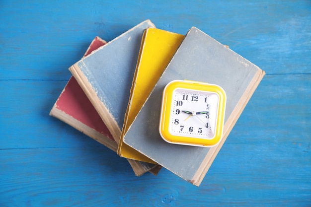 Gele klok en boeken op blauwe houten tafel.