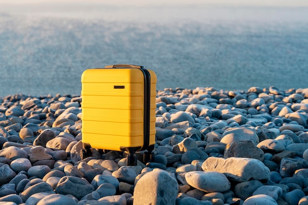 Gele koffer met een oranje sjaal aan de kust tegen de zee Reisconcept