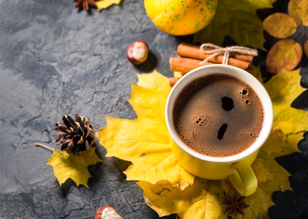 Gele koffiemok op donkere stenen tafel met herfstbladeren en kaneelstokjes