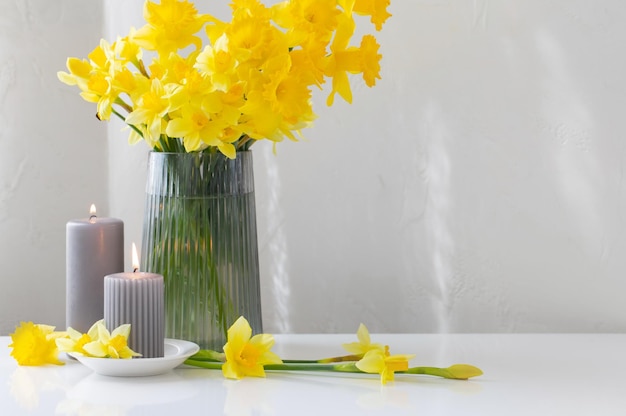 Gele lente narcissen in glazen vaas met brandende kaarsen op witte achtergrond