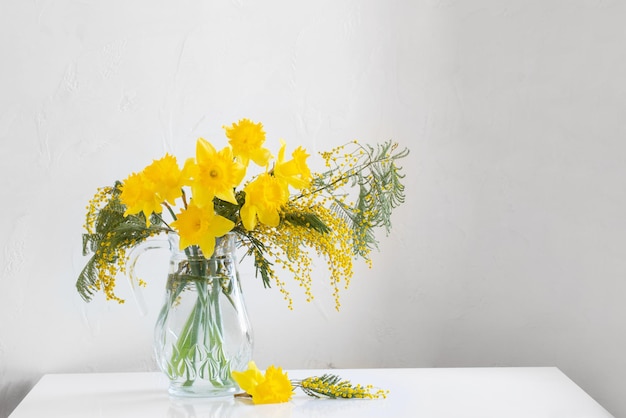 Gele Lentebloemen in glazen vaas op witte achtergrond