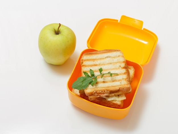 Gele lunchbox met geroosterde sneetjes brood, kaas en groene peterselie.