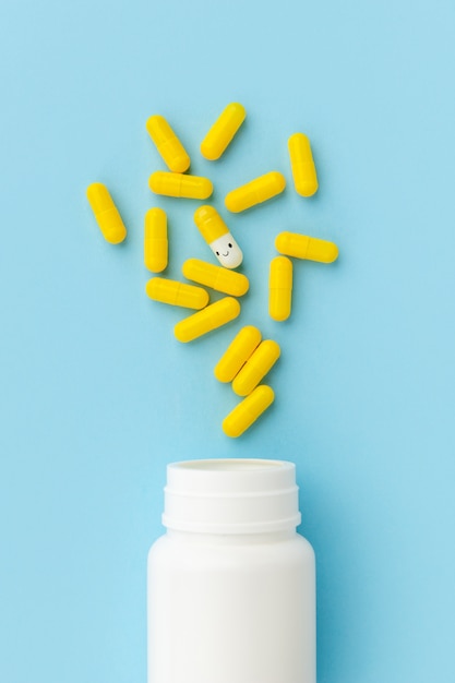 Gele medische pillen die uit een drugfles morsen op blauwe oppervlakte