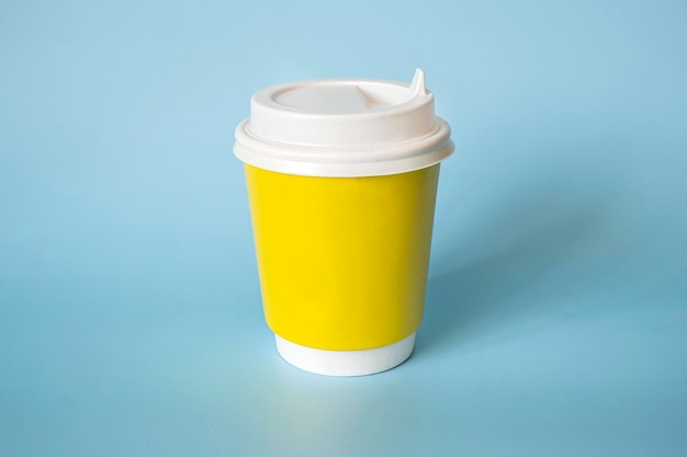 Gele papieren koffiemok op een blauwe achtergrond Lege ruimte voor tekst en ontwerp op een kopje koffie Het formulier voor de naam van de koffie of het bedrijf of de coffeeshop