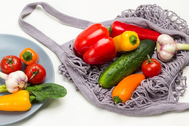 Gele paprika, knoflook en rode tomaten op grijze plaat. komkommers en paprika's in grijs gaas. witte achtergrond. bovenaanzicht