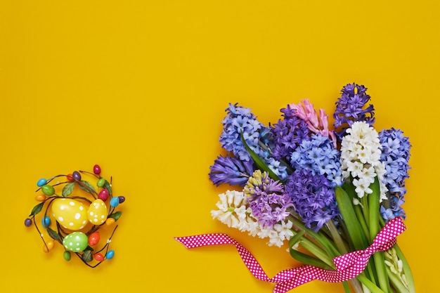 Gele Pasen-achtergrond. Lentebloemen en decoratieve paaseieren. Kopieer ruimte, bovenaanzicht. Pasen viering concept.