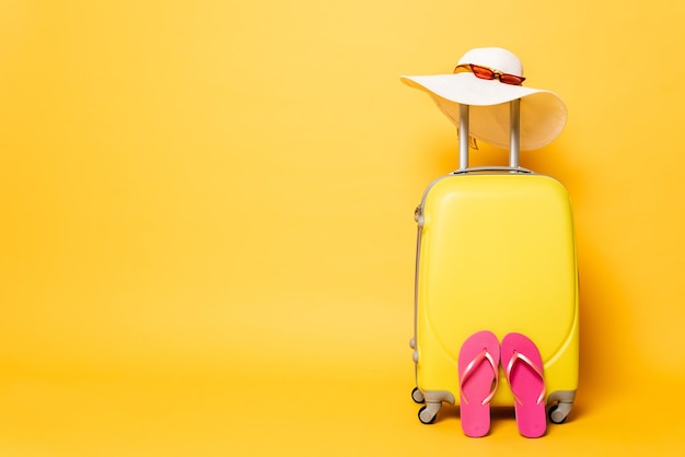 Foto gele reistas met slippers zonnehoed en zonnebril geïsoleerd op geel