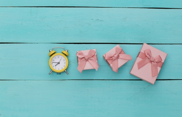 Gele retro wekker en geschenkdozen op blauwe houten achtergrond.