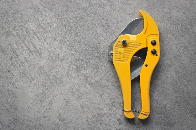 Gele schaar voor het snijden van pvc-kunststofbuizen op grijze achtergrond met kopieerruimte