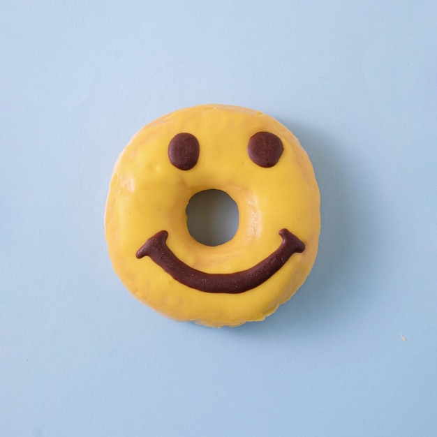 Gele smiley donut met glazuur op een blauwe pastel achtergrond. minimaal voedselconcept. plat leggen.