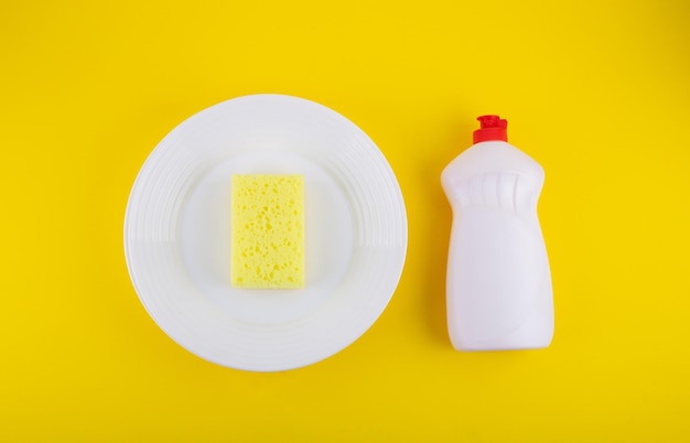 Gele spons schoonmaken op een witte plaat en afwasmiddel voor gerechten gele achtergrond Bovenaanzicht flatlay