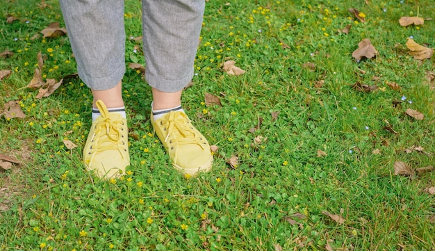 Gele sportschoenen met veters op een groene weide met gras en lentebloemen Het concept van de reistijd van de lente de benen van een volwassen vrouw in gele sneakers op een weide met kopieerruimte