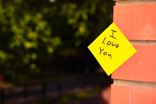 Foto gele sticker met het opschrift i love you geplakt op een bakstenen muur