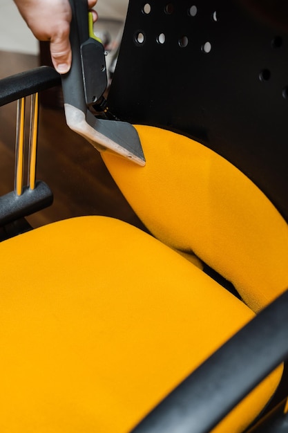 Foto gele stoel schoonmaken met was-stofzuiger-extractiemachine voor chemisch reinigen van gestoffeerde meubels huishoudster haalt vuil uit de fauteuil met behulp van een stomerij-extractor