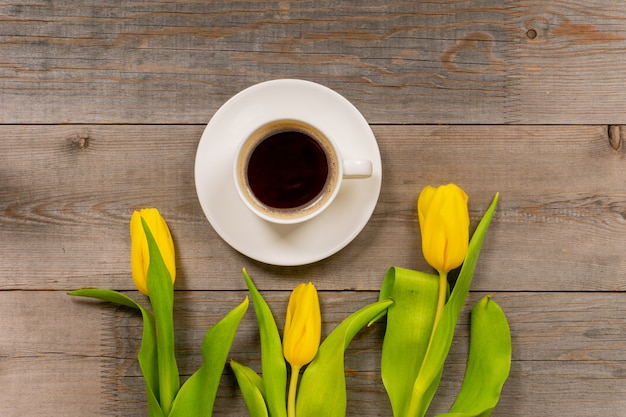 Gele tulpen en koffiekopje op rustieke houten tafel. Bovenaanzicht met kopie ruimte.