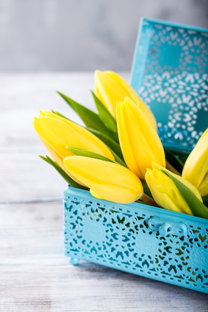 Gele tulpen in een blauwe metalen doos op het lichtgrijze oppervlak. Een cadeau voor vrouwendag. Wenskaart voor Moederdag. Kopieer ruimte