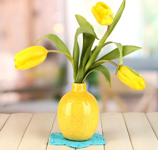 Gele tulpen in vaas op houten tafel op kamer achtergrond