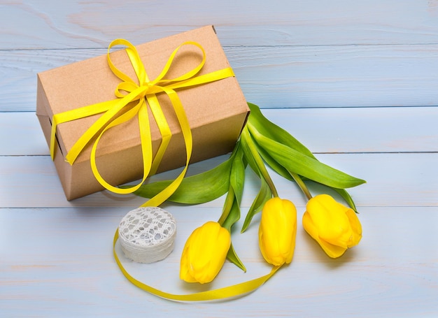 Gele tulpen op een geschenkdoos met een lint en op een achtergrond van natuurlijk hout Moederdag Valentijnsdag Wenskaart met plaats voor tekst