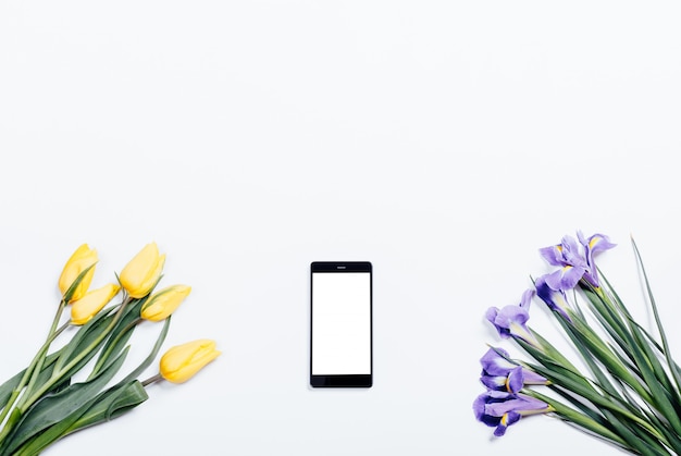 Gele tulpen, paarse irissen en mobiele telefoon op een witte achtergrond