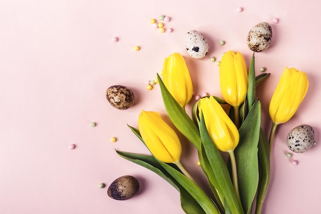 Gele tulpenbloemen en kwarteleitjes op pastelroze achtergrond.