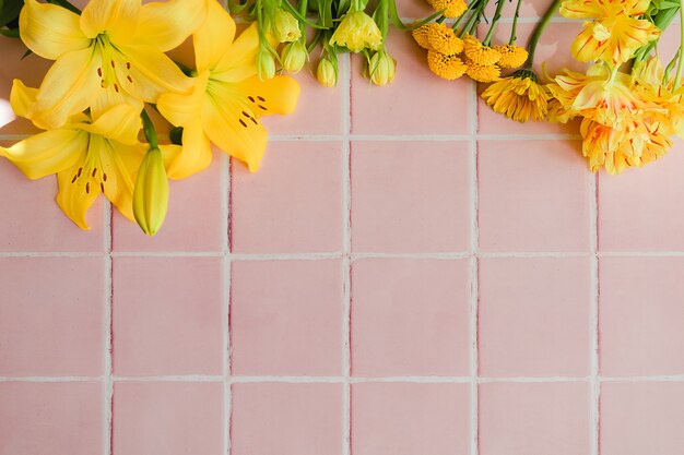 Gele verschillende bloemen op een roze tegelvloerachtergrond